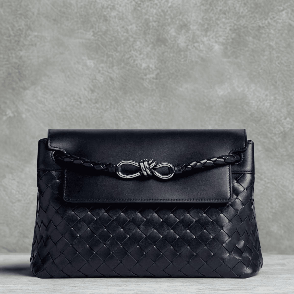 Close-up of a black Bottega Veneta Andiamo braided leather bag against a minimalist grey textured background, serving as the hero banner for The Wishline's designer brands collection.
