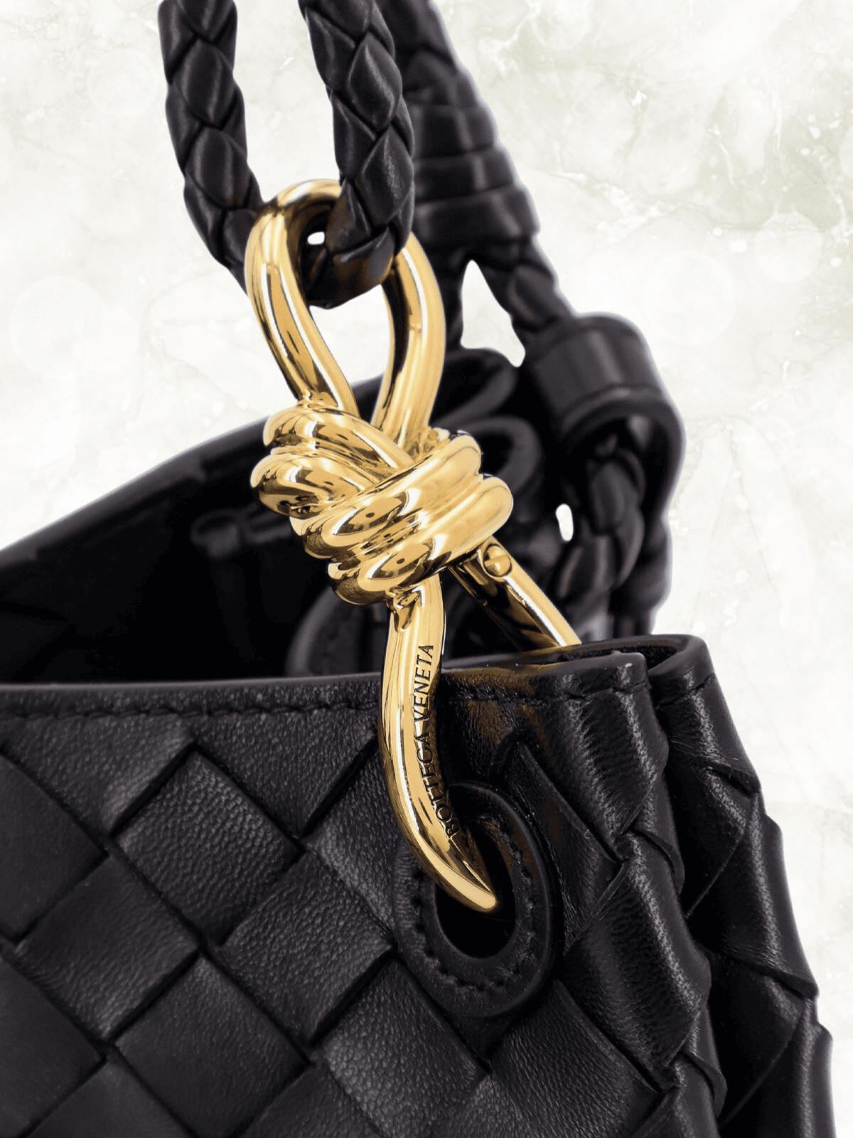 Close-up of Bottega Veneta black woven leather bag with gold knot hardware detail.