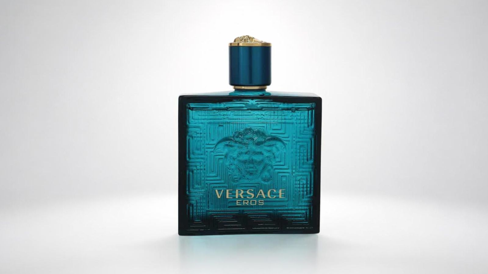 Versace Eros aftershave lotion bottle featuring its iconic turquoise blue glass design with the raised Medusa head motif and Greek key border for THE WISHLINE luxury men's after shave and grooming collection navigation.