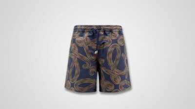 Navy blue swim shorts featuring an allover tan abstract swirling rope pattern, an elastic drawstring waistband, and metal aglets for THE WISHLINE luxury men's beachwear and swimwear collection navigation.