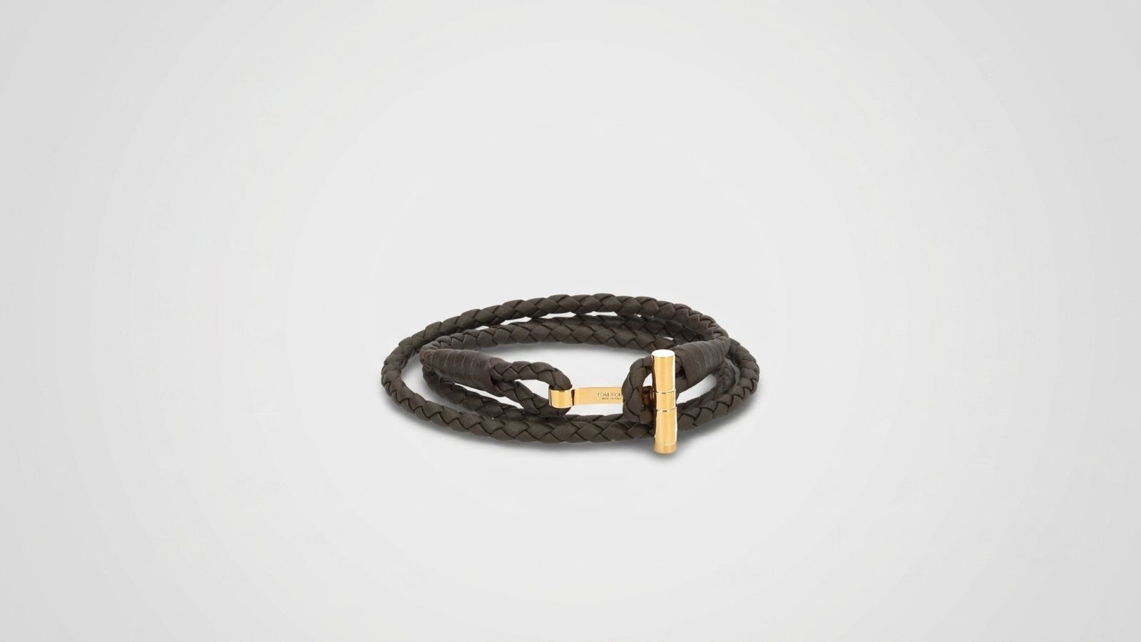 Tom Ford dark brown braided leather wrap bracelet featuring a polished gold-tone T-bar clasp closure for THE WISHLINE luxury men's jewellery collection navigation.