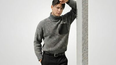 Grey marl heavy-knit turtleneck sweater featuring a contrast black leather chest pocket, tucked into black trousers with a matching leather belt for THE WISHLINE luxury men's knitwear and sweaters collection navigation.