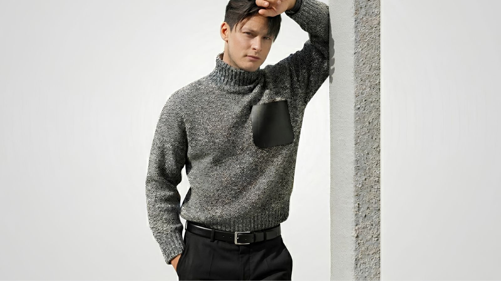 Grey marl heavy-knit turtleneck sweater featuring a contrast black leather chest pocket, tucked into black trousers with a matching leather belt for THE WISHLINE luxury men's knitwear and sweaters collection navigation.