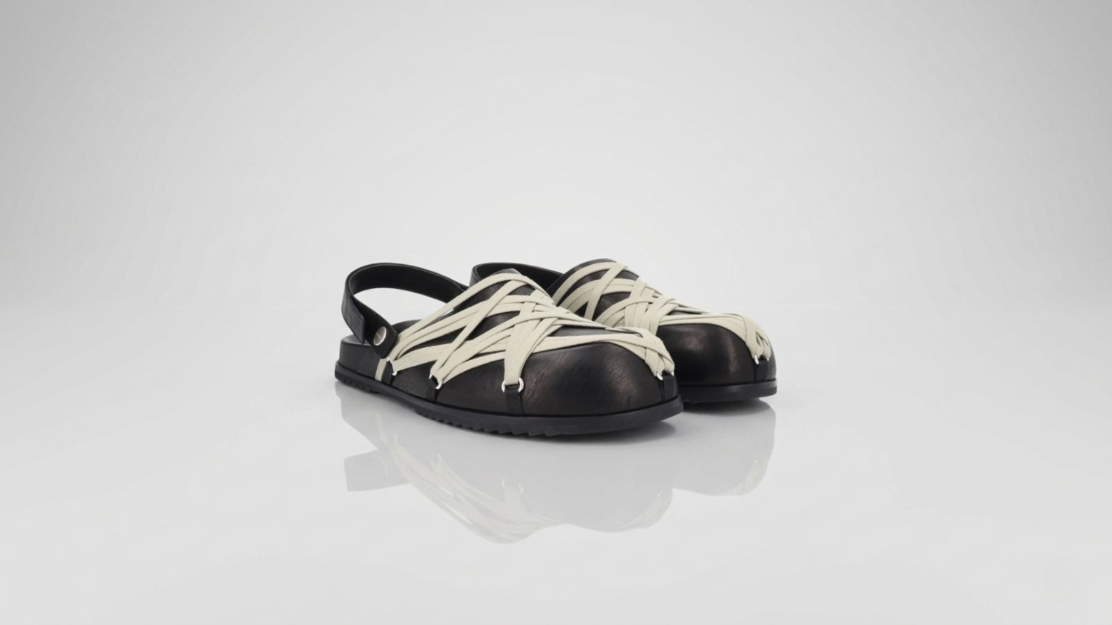 Black leather slingback sandals featuring an intricate off-white lace-up cage design over a rounded toe for THE WISHLINE luxury men's sandals and flats collection navigation.