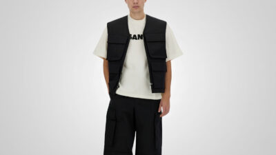 Black multi-pocket utility vest layered over a white graphic T-shirt and paired with black cargo trousers for THE WISHLINE luxury men's vests and gilets collection navigation.