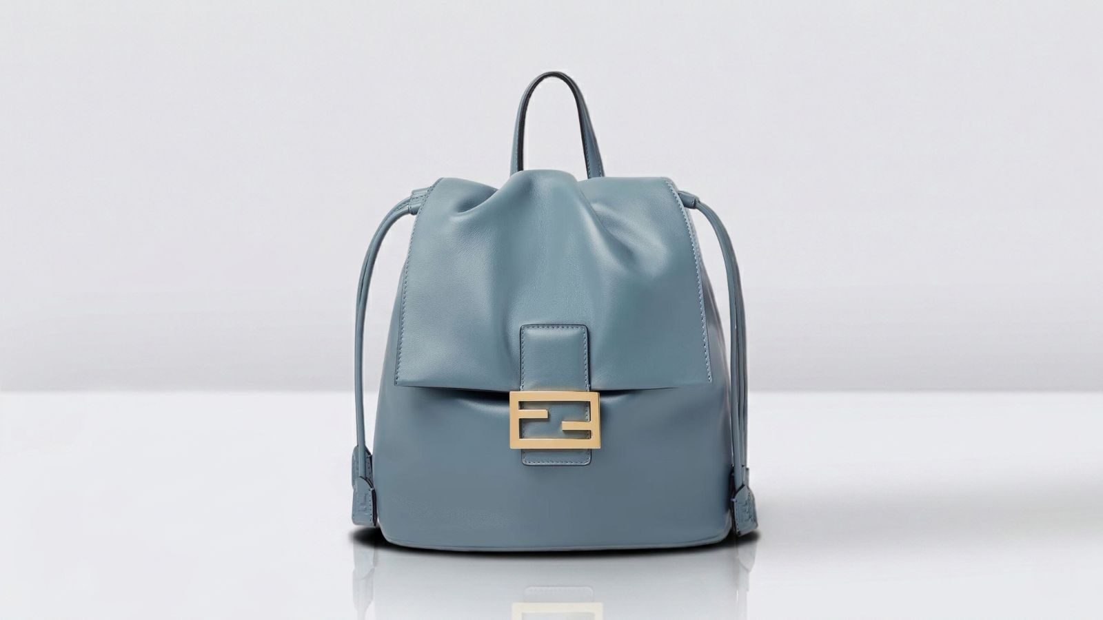 Fendi light blue leather drawstring backpack featuring a gold FF baguette buckle detail for THE WISHLINE luxury women's backpack collection navigation.