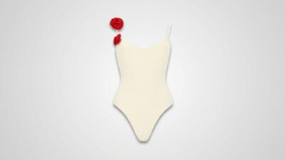 Elegant off-white one-piece swimsuit featuring a sweetheart neckline, thin spaghetti straps, and two vibrant red 3D rosette floral accents on the right shoulder for THE WISHLINE luxury women's beachwear and designer swimwear collection navigation.