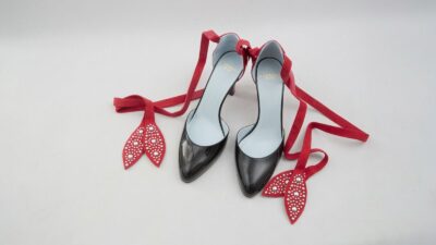 Valentino Garavani black patent leather pumps featuring red suede ankle tie straps with studded leaf accents for THE WISHLINE luxury women's heels collection navigation.