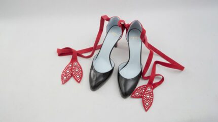 Valentino Garavani black patent leather pumps featuring red suede ankle tie straps with studded leaf accents for THE WISHLINE luxury women's heels collection navigation.