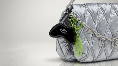 Diesel black patent leather micro bag charm and neon green 1DR logo keychain clipped to a quilted metallic silver shoulder bag for THE WISHLINE luxury keychains collection navigation.