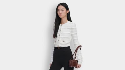 Model styling a white textured ruffle knit cardigan with jewel buttons and black trousers for THE WISHLINE luxury women's knitwear navigation.