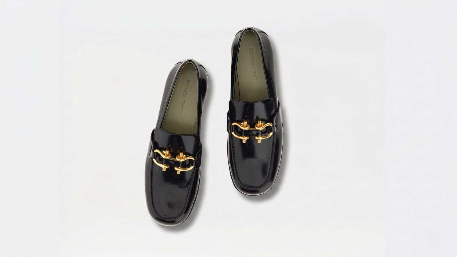 Bottega Veneta black patent leather loafers featuring prominent gold bit hardware details for THE WISHLINE luxury women's loafers collection navigation.
