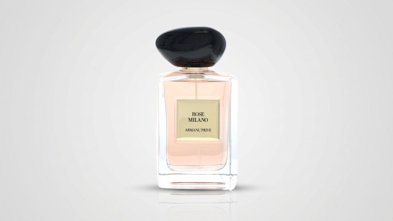 Clear rectangular glass perfume bottle filled with soft pink liquid, featuring a gold square label and topped with an organic, smooth black pebble-shaped cap for THE WISHLINE luxury women's parfum testers and designer fragrance collection navigation.