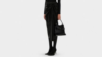 Model styling a flowing high-waisted black midi skirt with an asymmetrical hemline for THE WISHLINE luxury women's skirts navigation.