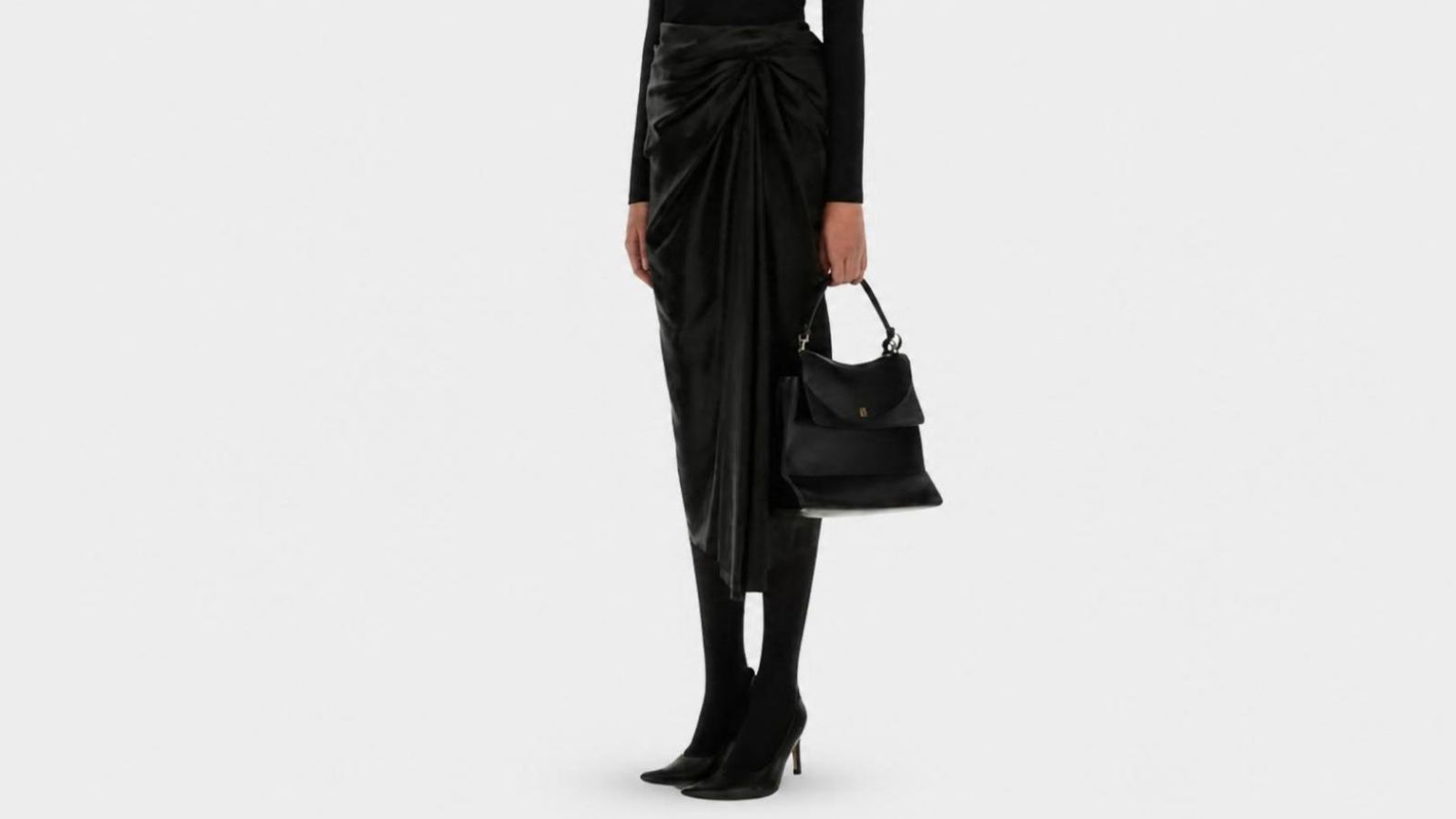 Model styling a flowing high-waisted black midi skirt with an asymmetrical hemline for THE WISHLINE luxury women's skirts navigation.