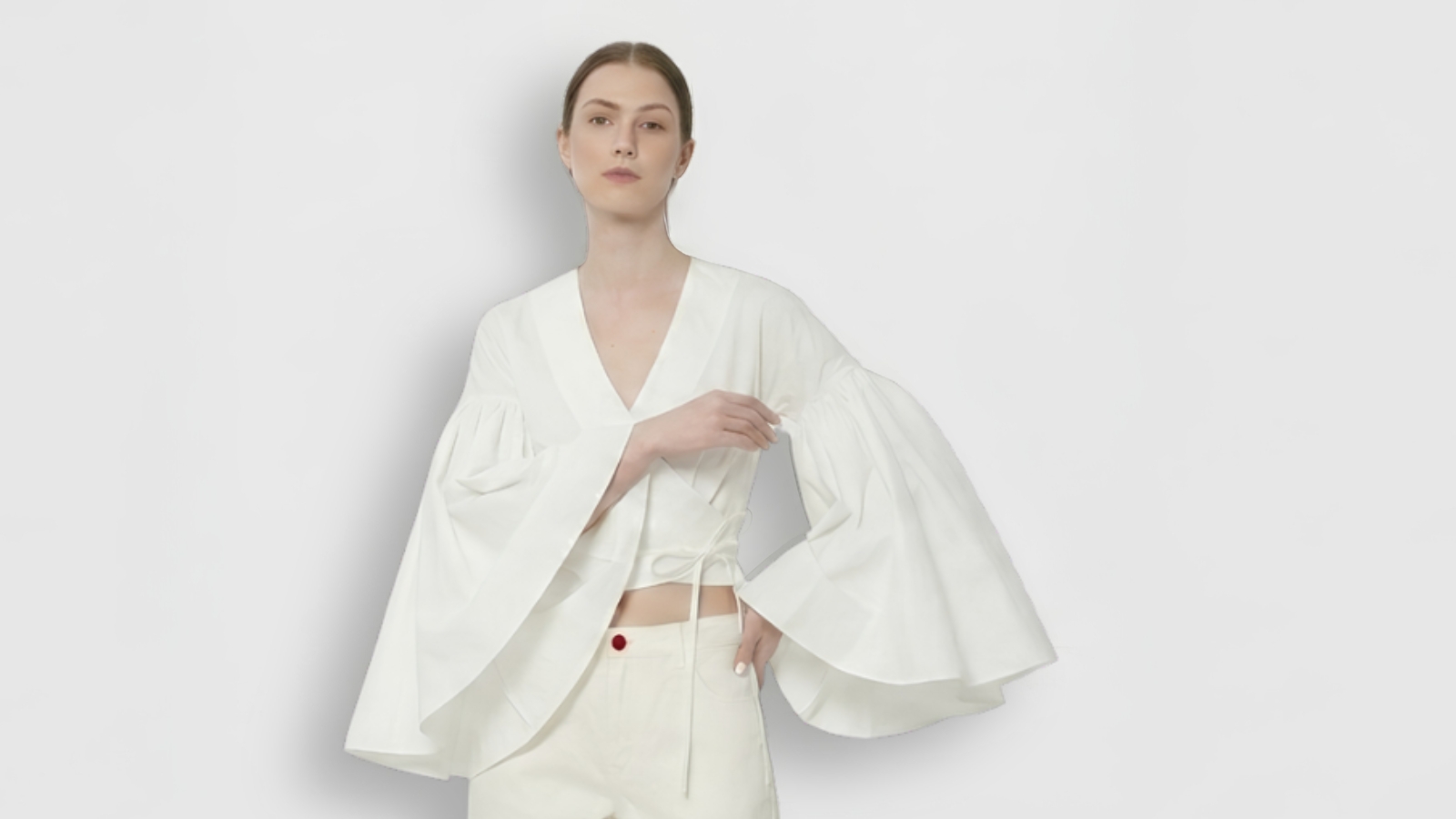 Model styling a structured white wrap blouse featuring dramatic wide bell sleeves for THE WISHLINE luxury women's tops category navigation.
