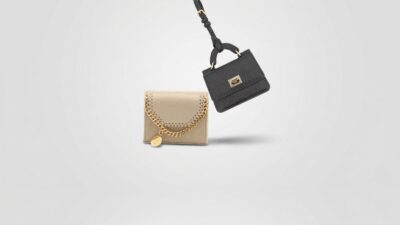 Stella McCartney beige Falabella trifold wallet with gold chain trim alongside a black Dolce & Gabbana micro bag charm for THE WISHLINE designer women's wallets and accessories navigation.