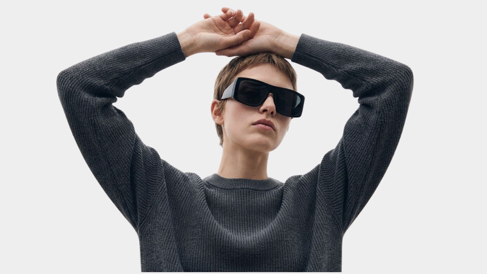 Model wearing oversized black designer sunglasses and a grey knit sweater for THE WISHLINE luxury accessories category navigation.