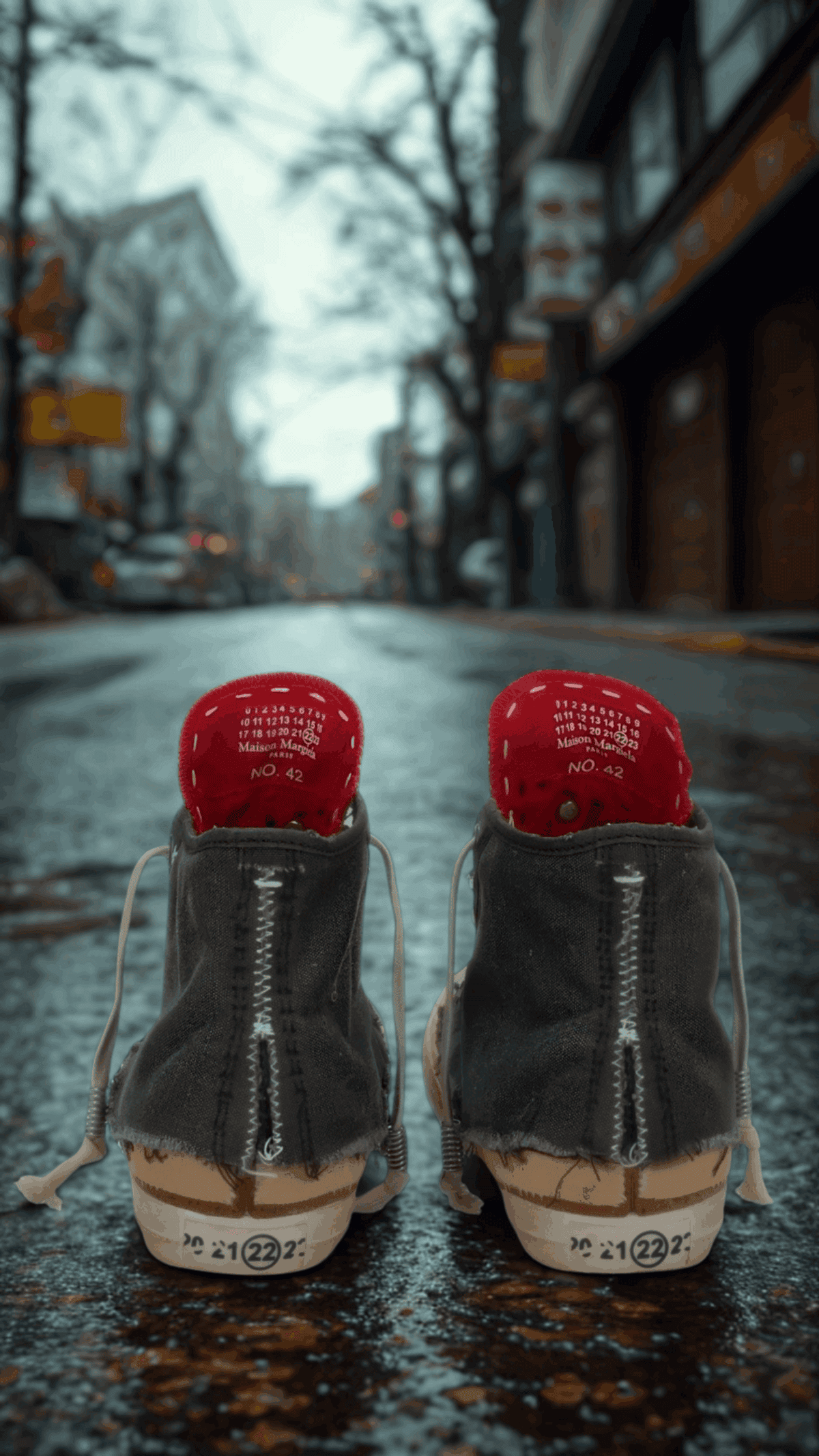 Pair of Maison Margiela “Loved to Death” sneakers with red heel tabs displayed on a city street, symbolizing worn luxury and contemporary urban style — men’s designer sneakers collection at THE WISHLINE.