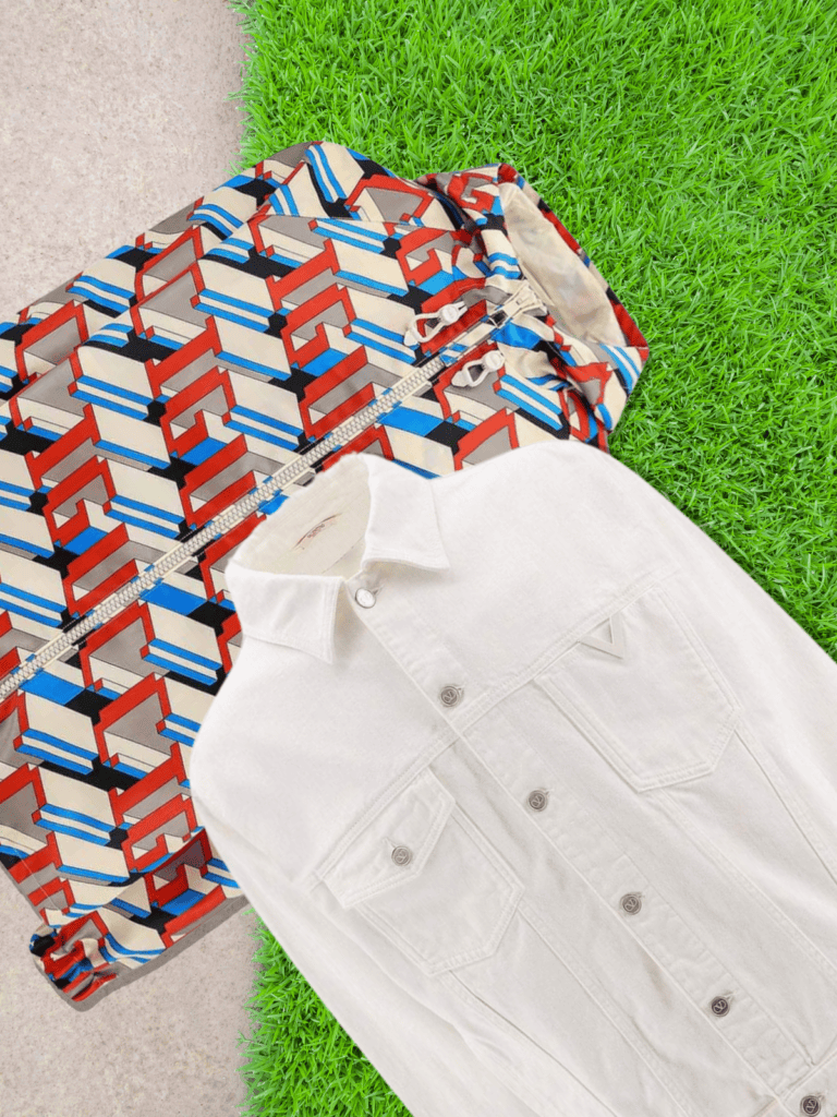 A patterned windbreaker and a white denim jacket laid on grass and stone, showcasing a mix of bold prints and timeless essentials.
