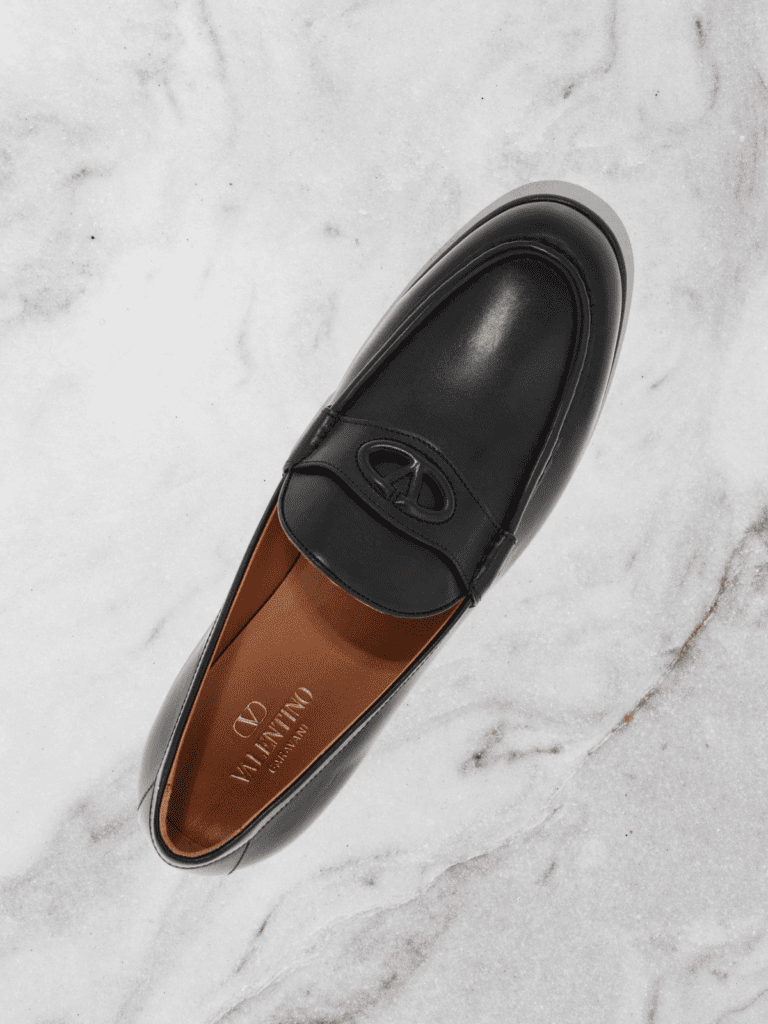 A sleek black leather loafer displayed on a marble surface, embodying timeless craftsmanship and sophistication.