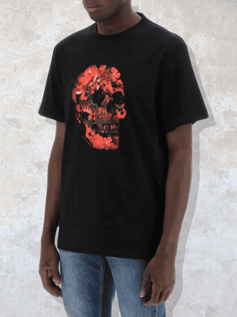 A model wearing a black graphic T-shirt featuring a striking red floral skull design, paired with denim for a modern edge.