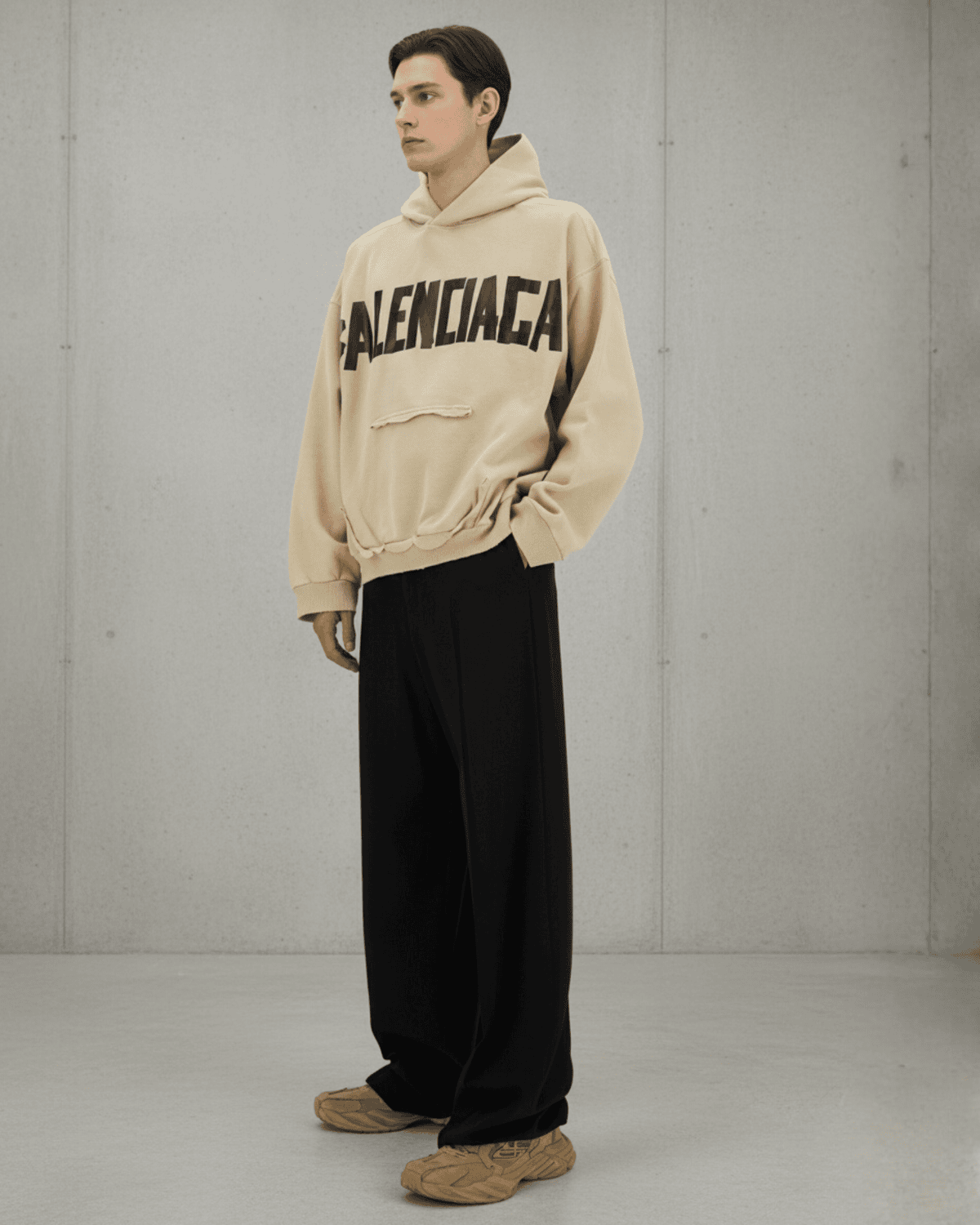 Model wearing a beige Balenciaga hoodie with black wide-leg trousers and sneakers, styled against a minimalist concrete backdrop — featured in THE WISHLINE Men’s Clothing Seasonal Offers edit.