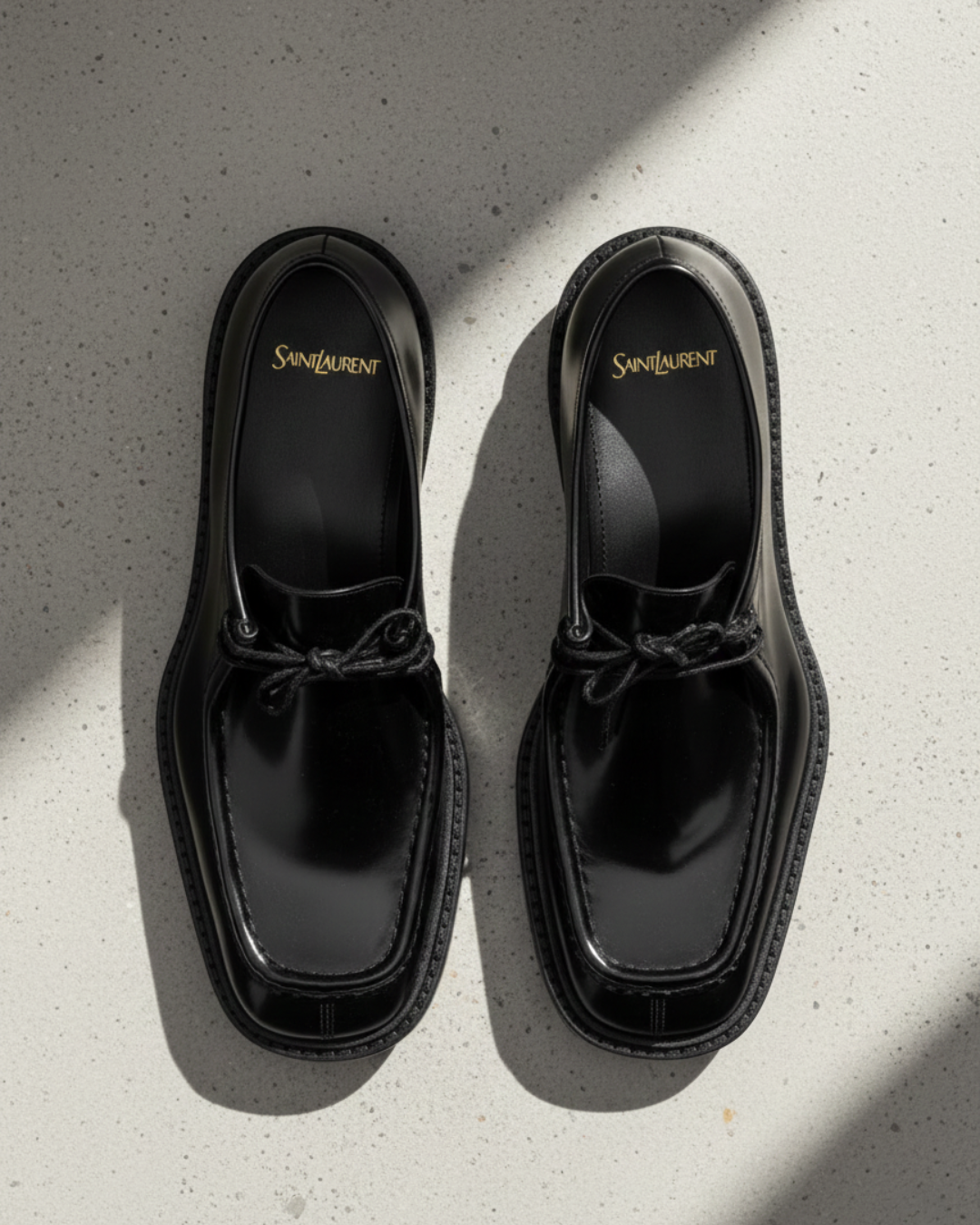 Black patent leather Saint Laurent loafers displayed on a light stone surface, featured in THE WISHLINE Men’s Seasonal Offers collection.