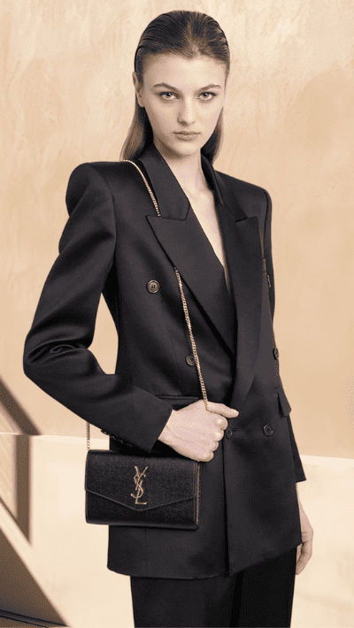Woman model wearing a black Saint Laurent suit and holding a black YSL shoulder bag.