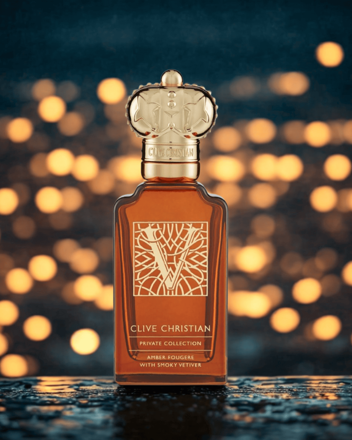 Clive Christian Private Collection Amber Fougere perfume bottle with gold crown cap placed on a reflective surface, illuminated by warm bokeh lights — representing THE WISHLINE Men’s Luxury Line Up.