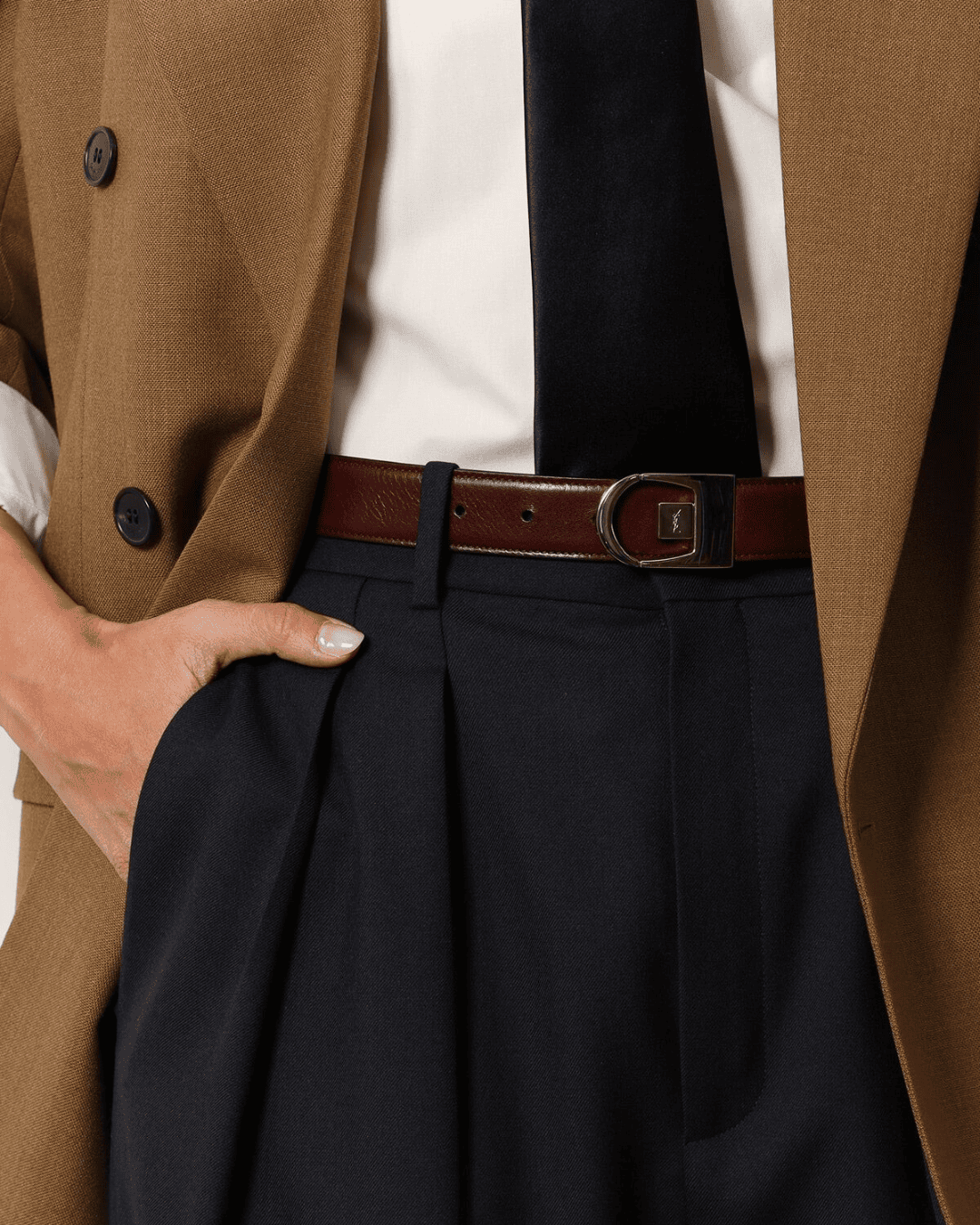 Close-up of a tailored camel blazer and dark pleated trousers with a leather belt, representing the personalized and curated shopping experience on THE WISHLINE.