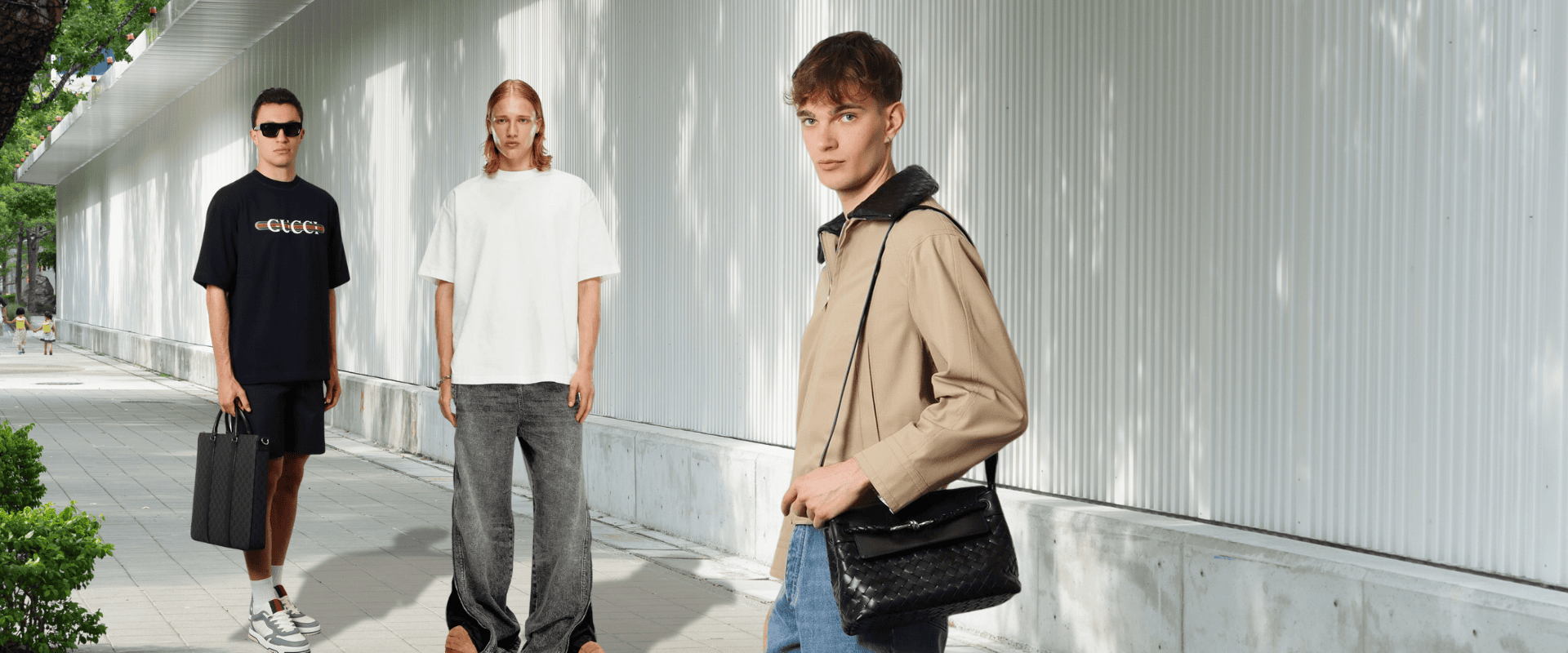 Three men in stylish designer outfits and bags walking outdoors in daylight — showcasing curated luxury menswear from top fashion brands.