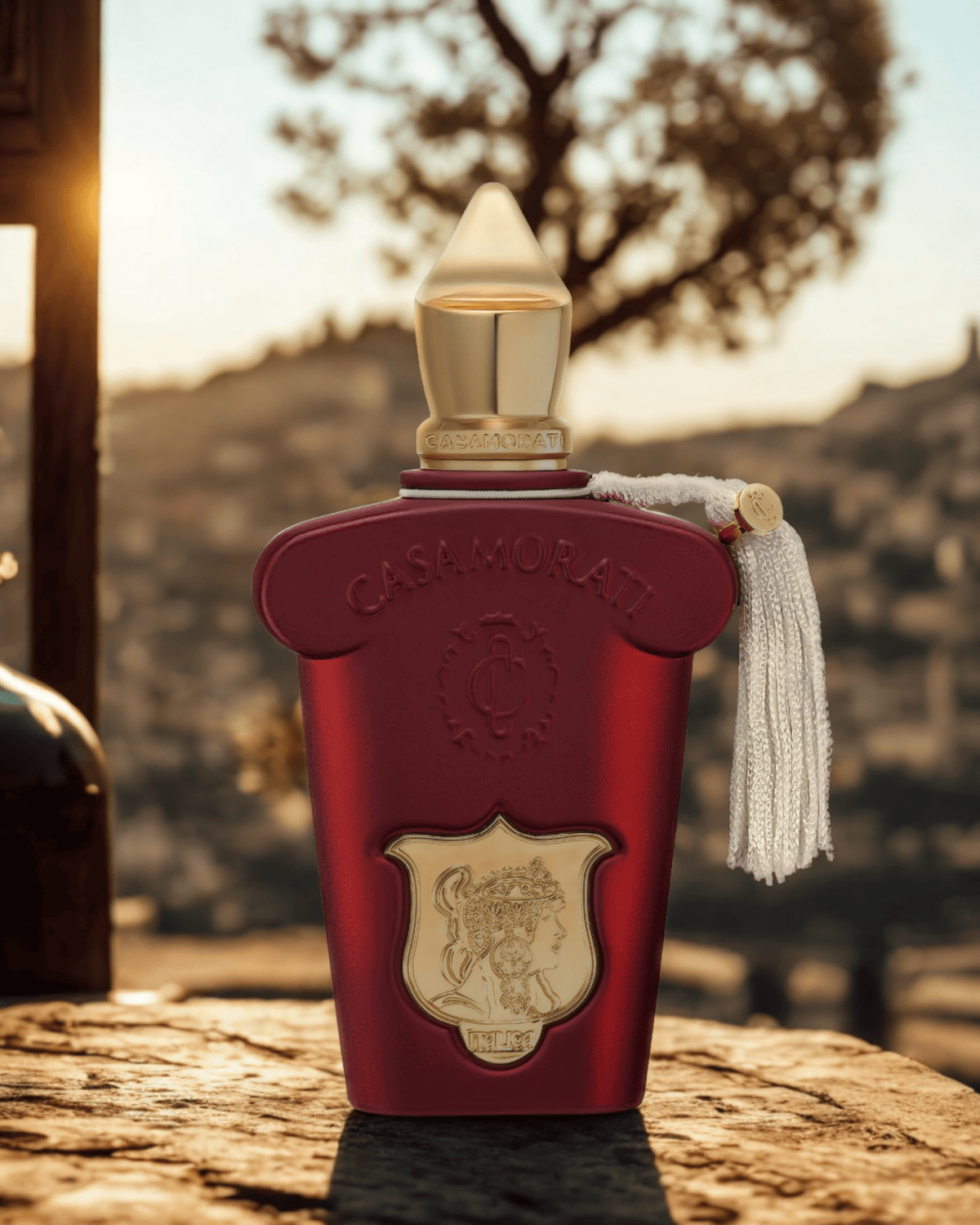 Xerjoff Italica perfume bottle on a rustic Italian table at sunset, surrounded by warm tones reflecting creamy almond and vanilla notes.